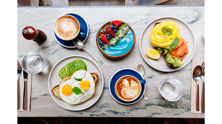 Brunch at cafe with avocado toast, fried and scrambled egg, salmon, smoothie bowl and coffee