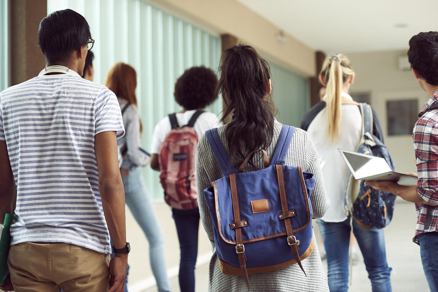 Students walking in school corridor, rear view