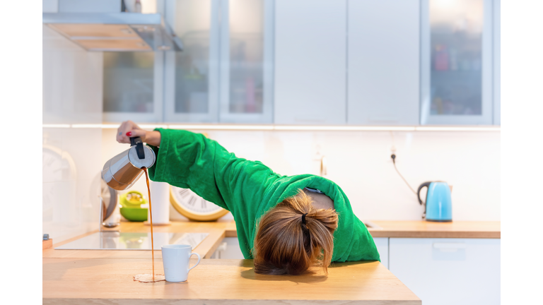 Tired woman sleeping on the table in the kitchen at breakfast. Trying to drink morning coffee
