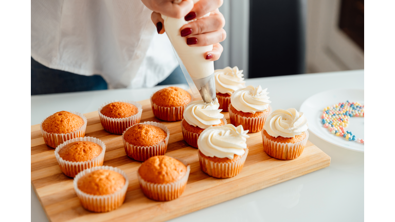 Woman decorates freshly baked cupcakes with cream