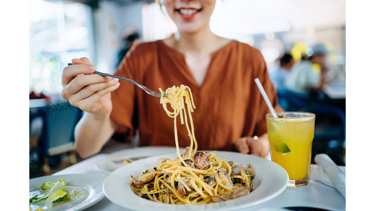 Close up of young Asian woman eating freshly served linguine pasta with fresh clams for lunch in a restaurant. Eating out lifestyle