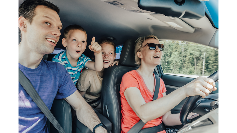 Amazing journey of a happy young family with playful children by car during a tourist trip. The little son emotionally points a finger forward. Inside view