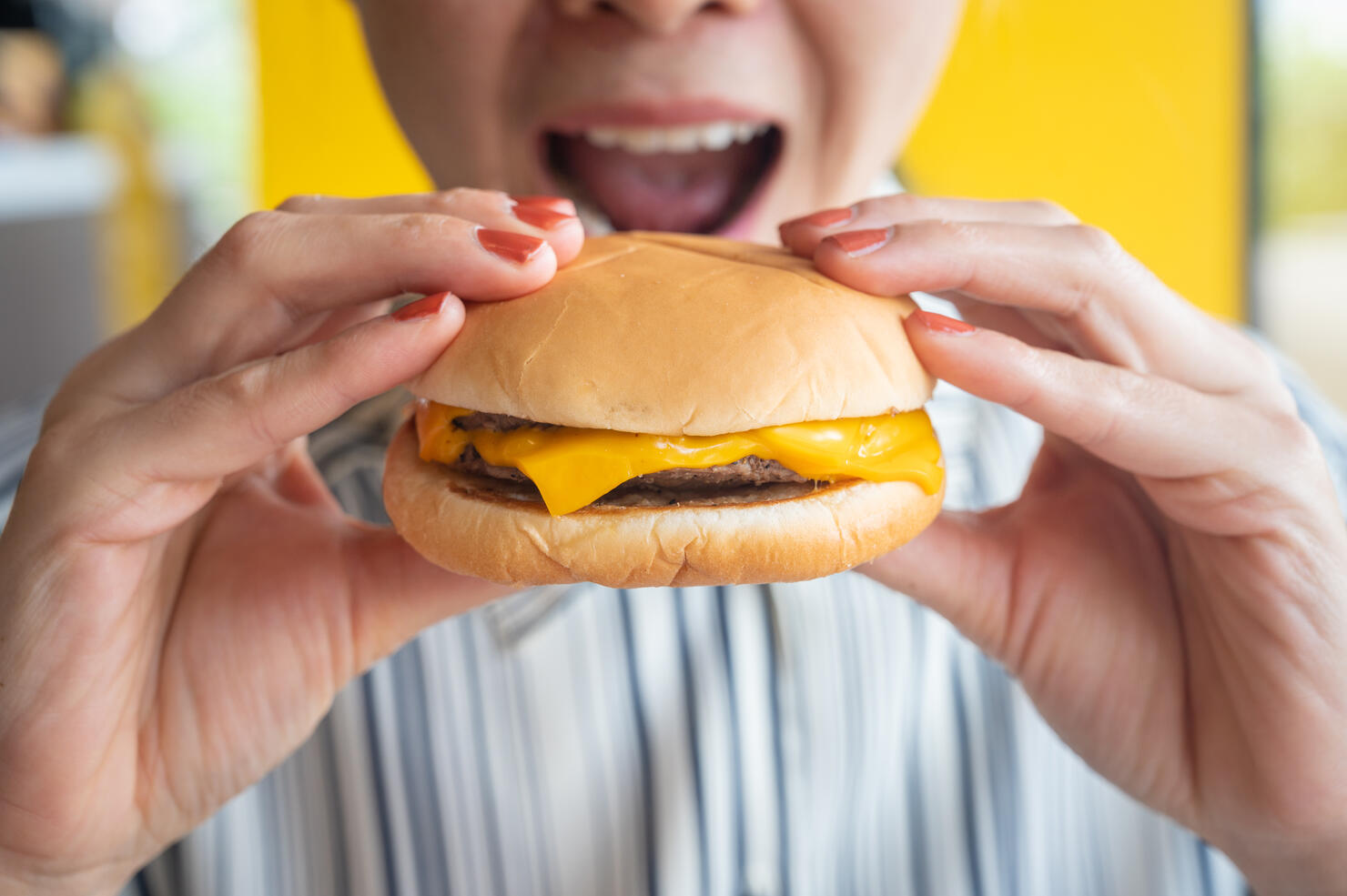 Close up of woman opened her mouth to eat a cheese burger.