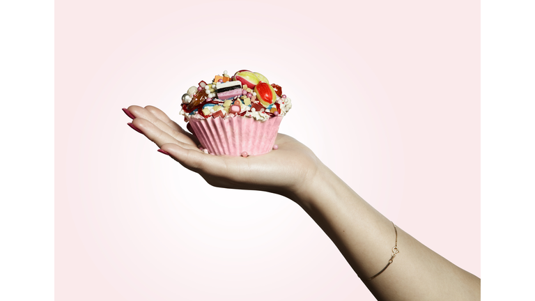Hand holding pink designed cupcake full of sweets