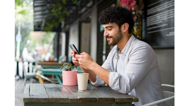 Happy man drinking checking his cell phone at a coffee shop while drinking a cappuccino