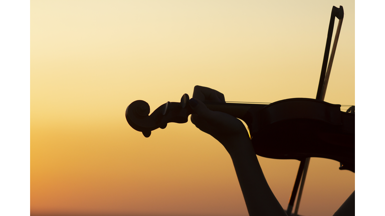 silhouette of a wooden violin in female hands, the figure of a stringed musical instrument on a sunset sky, the concept of music and art