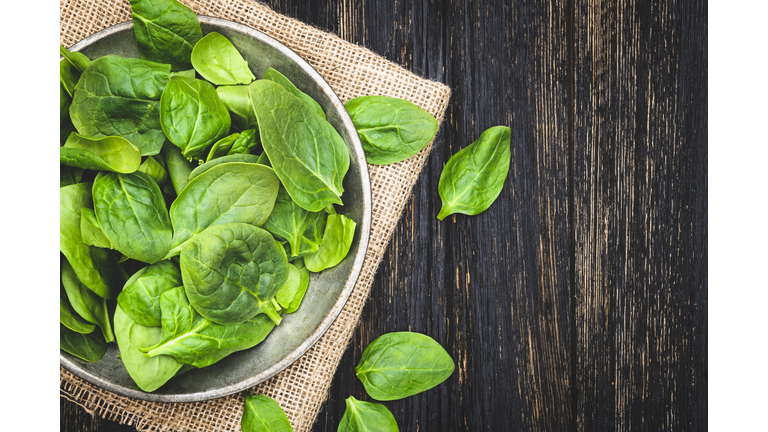 Fresh spinach leaves in bowl on rustic wooden table