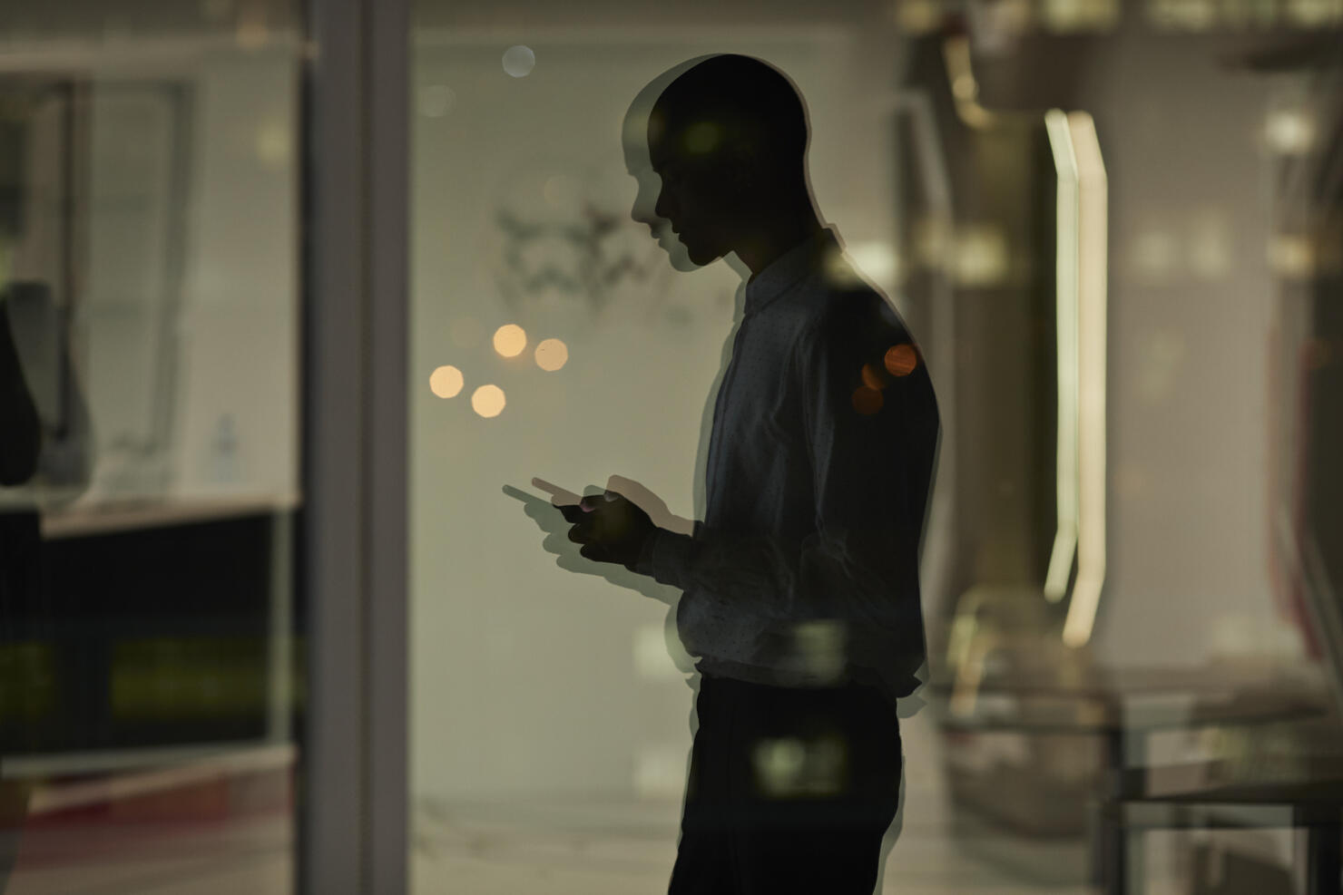 Reflection of young businessman checking phone inside office at nighttime