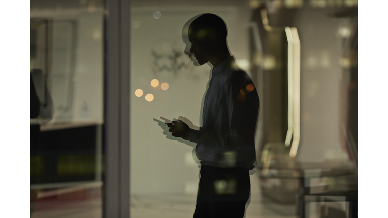 Reflection of young businessman checking phone inside office at nighttime