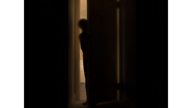 silhouette of person peeking into dark room through a cracked door