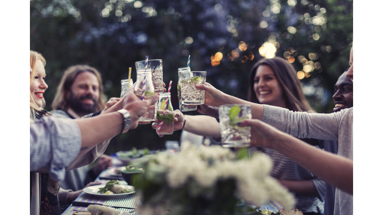 Multi-ethnic friends toasting mojito glasses at dinner table in yard