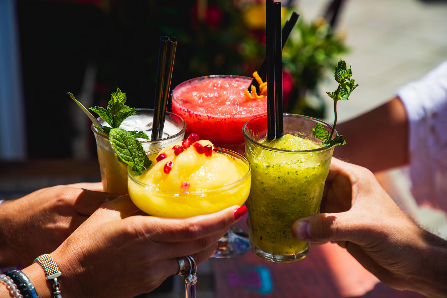 Four hands holding glasses with yellow and red fruit cocktails in a toast