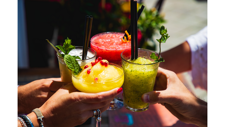 Four hands holding glasses with yellow and red fruit cocktails in a toast