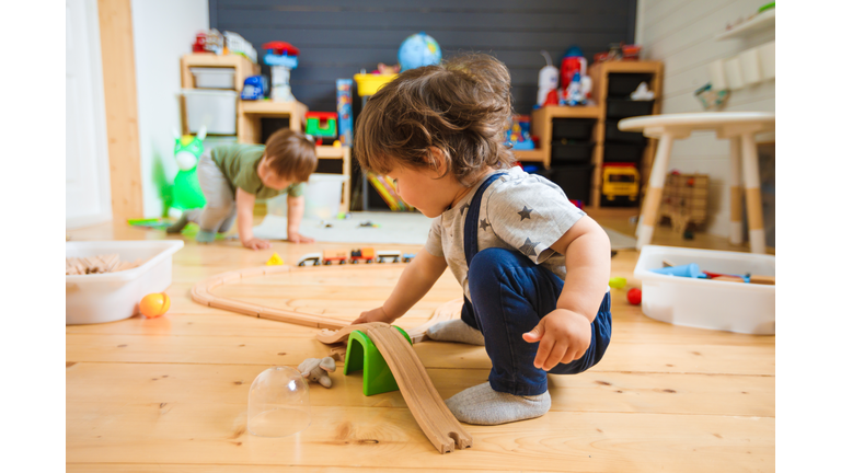 Little boys play with a wooden railroad in a stylish nursery.