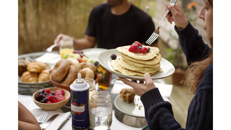 Young woman eating pancakes during breakfast with friends