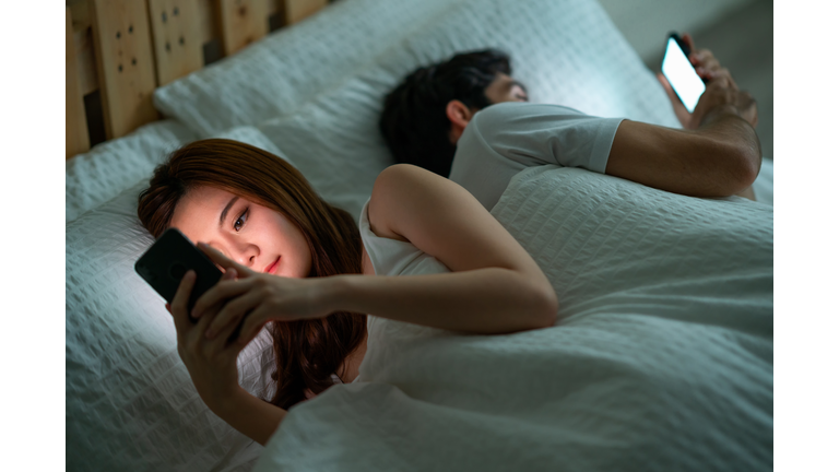 Shot of a young couple using their cellphones in bed at morning back to back