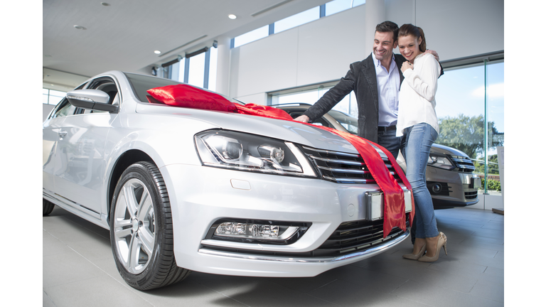 Man looking at new car with red bow with girlfriend in car dealership