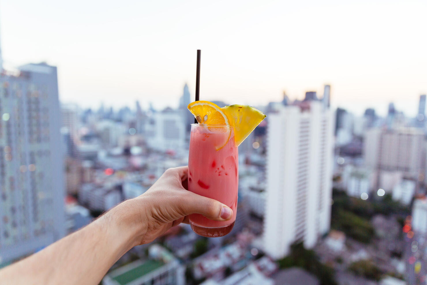 Drinking cocktail at the rooftop bar with city view, personal perspective view