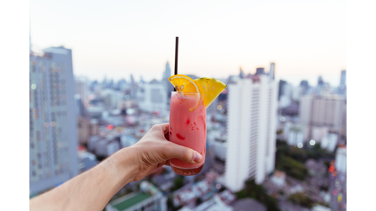 Drinking cocktail at the rooftop bar with city view, personal perspective view