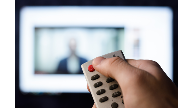 Irritated young man pushes red button on a remote controller in order to turn off a smart TV set with video in browser