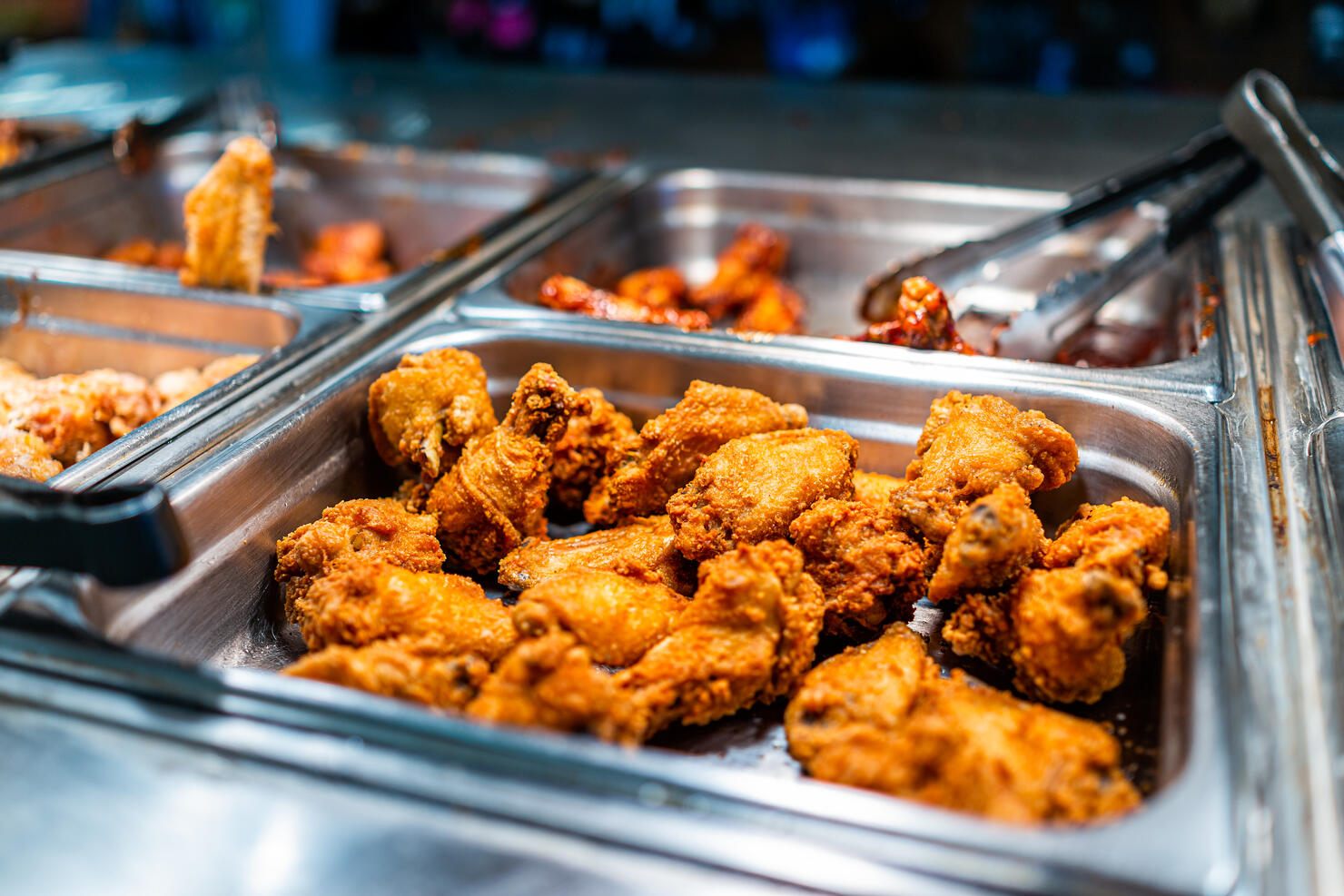 Fried chicken thighs buffet bar self serve with tongs in grocery store, restaurant or catering event with crisp skin and unhealthy food