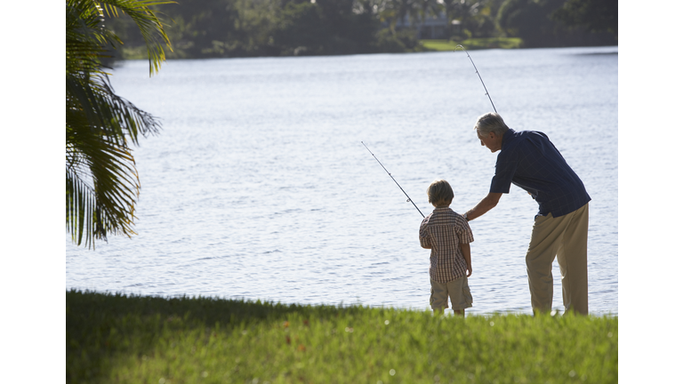 Man and young boy outdoors at park fishing in a lake