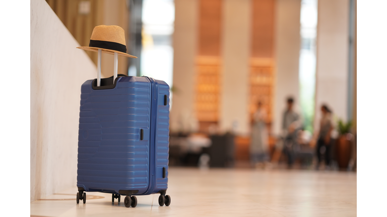 Luggage with sun hat placing in front of hotel lobby isolated over hotel reception blurred background