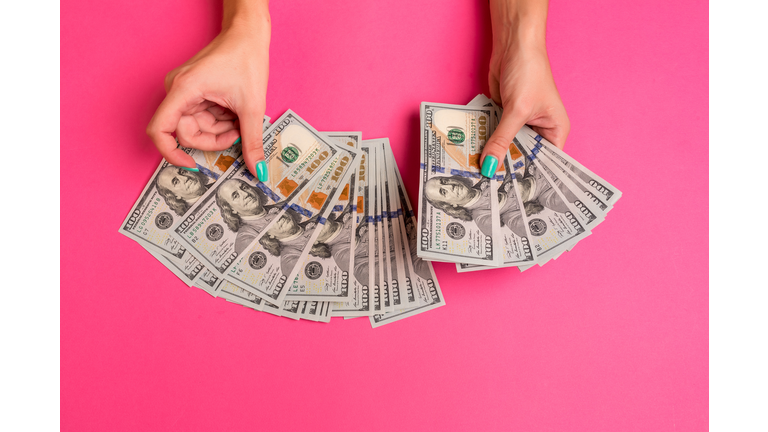 A woman is holding money in her hands. Pink background. Top view copy space