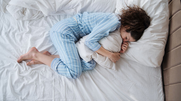 Top view of depressed woman in pajamas lying in bed in bedroom.