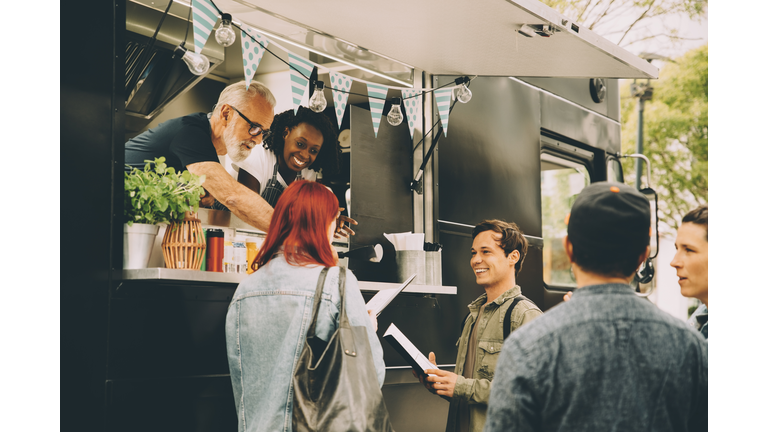 Owner with assistant talking to smiling customers by food truck