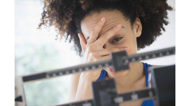 Mixed race woman hiding from weight on scale