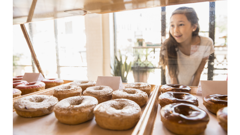 Mixed race girl examining donuts in bakery