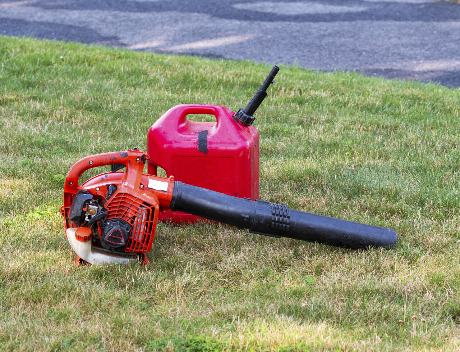 Red leaf blower and gas can on a residential lawn