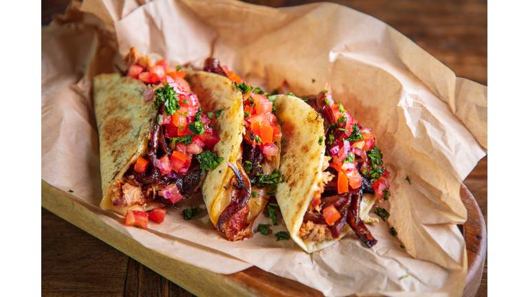 Serving of tacos with shredded roast pork and cheese filling on brown paper in wooden plate