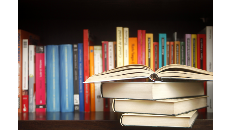 Row of books on a shelf, multicolored book spines, stack in the foreground..