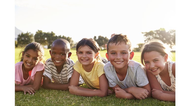Boys and girls lying on grass in Summer, looking to camera