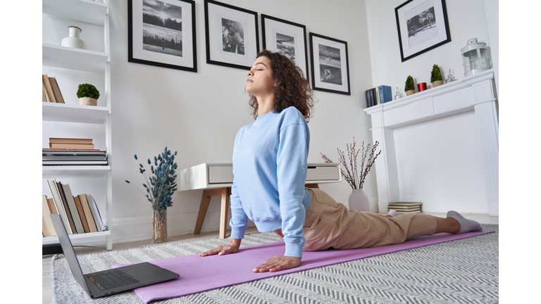 Fit young woman doing yoga exercise watching tv yoga class learning position with fitness tutorial on laptop computer stretching on mat at home, training body flexibility, online workout concept.