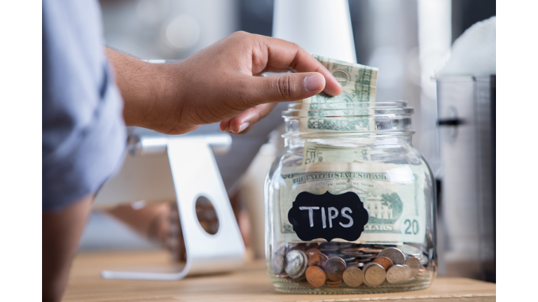 Coffee shop customer places cash in a tip jar