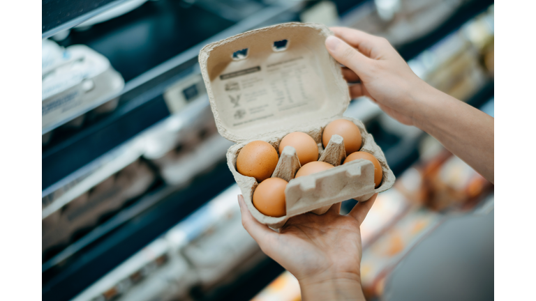 Close up of young Asian woman grocery shopping in a supermarket. She is holding a box of fresh organic free range eggs in front of a refrigerated section. Healthy eating lifestyle