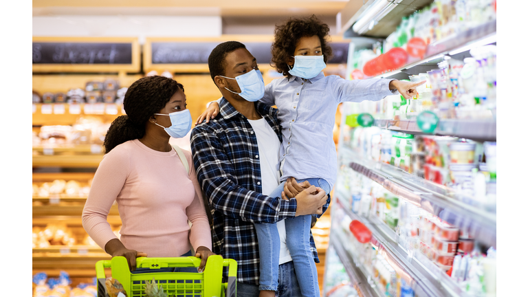 Family shopping during coronavirus pandemic. Black family with child wearing face masks, purchasing food at supermarket