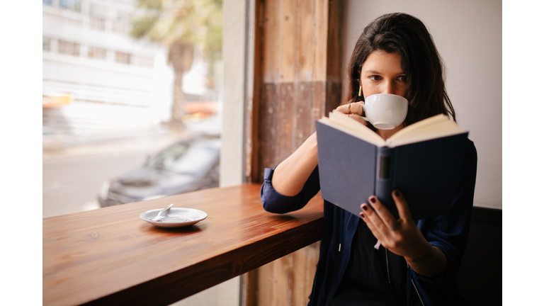 Girl Drinking Coffee and Reading Book in Cafe