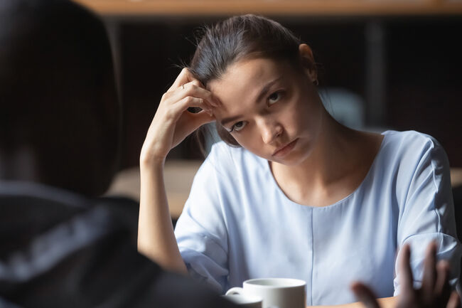 Bored unhappy girlfriend listening to African American boyfriend in cafe