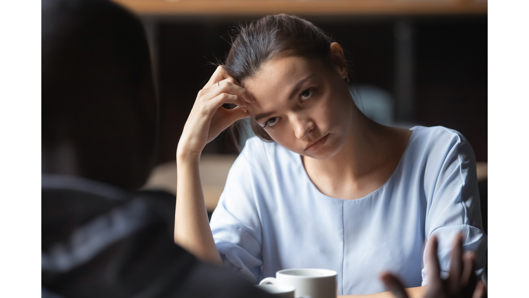 Bored unhappy girlfriend listening to African American boyfriend in cafe