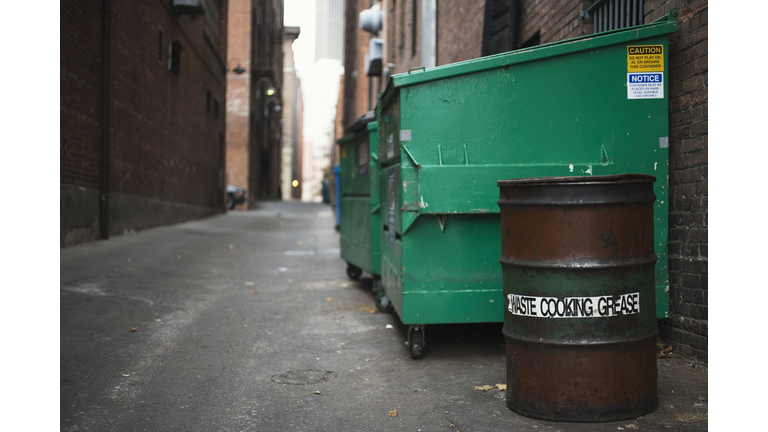 Garbage dumpsters and 'waste cooking grease' barrel  in alley