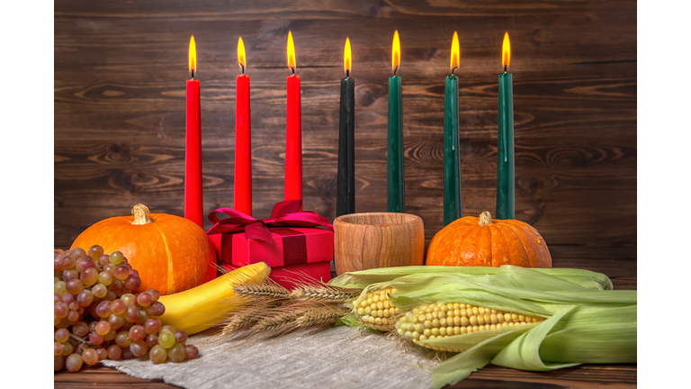 Kwanzaa festival concept with seven candles red, black and green, gift box, pumpkins, ears of wheat, grapes, corns, banana, bowl and fruits on wooden background, close up