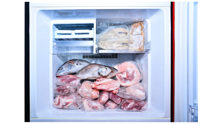 Many meat in refrigetator freezer isolated on white background. Closeup lot of raw pork, fish, meat and chicken in freezing compartment