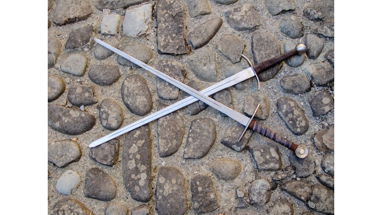 Two medieval swords, crossed, on cobblestone floor.