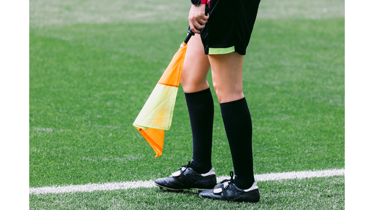 Soccer assistant linesman referee woman with the flag on the field of play, moving.