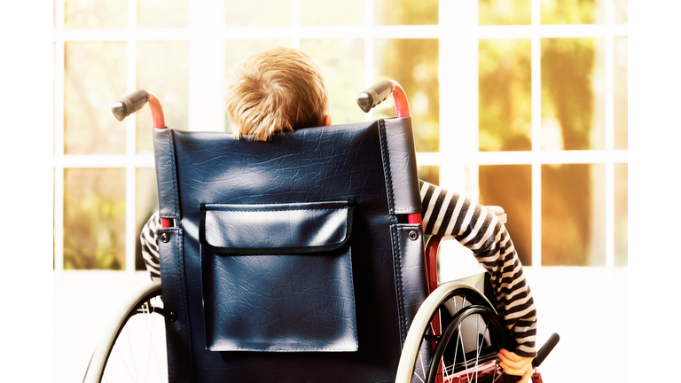 Little boy wheels his wheelchair towards sunny window