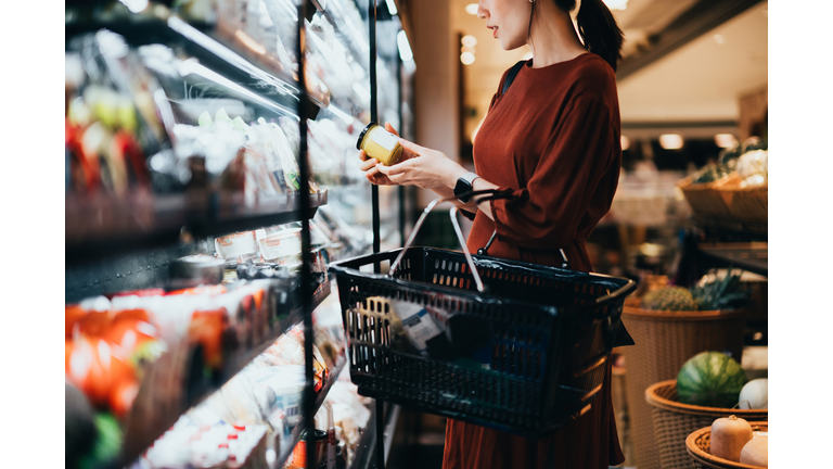 Cropped shot of young Asian woman carrying a shopping basket, standing along the dairy aisle, reading the nutrition label on the bottle of a fresh organic healthy yoghurt. Making healthier food choices